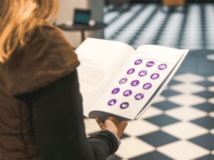 An over-the-shoulder view of a women in a brown jacket reading a brochure which has a series of purple icons on a white page.