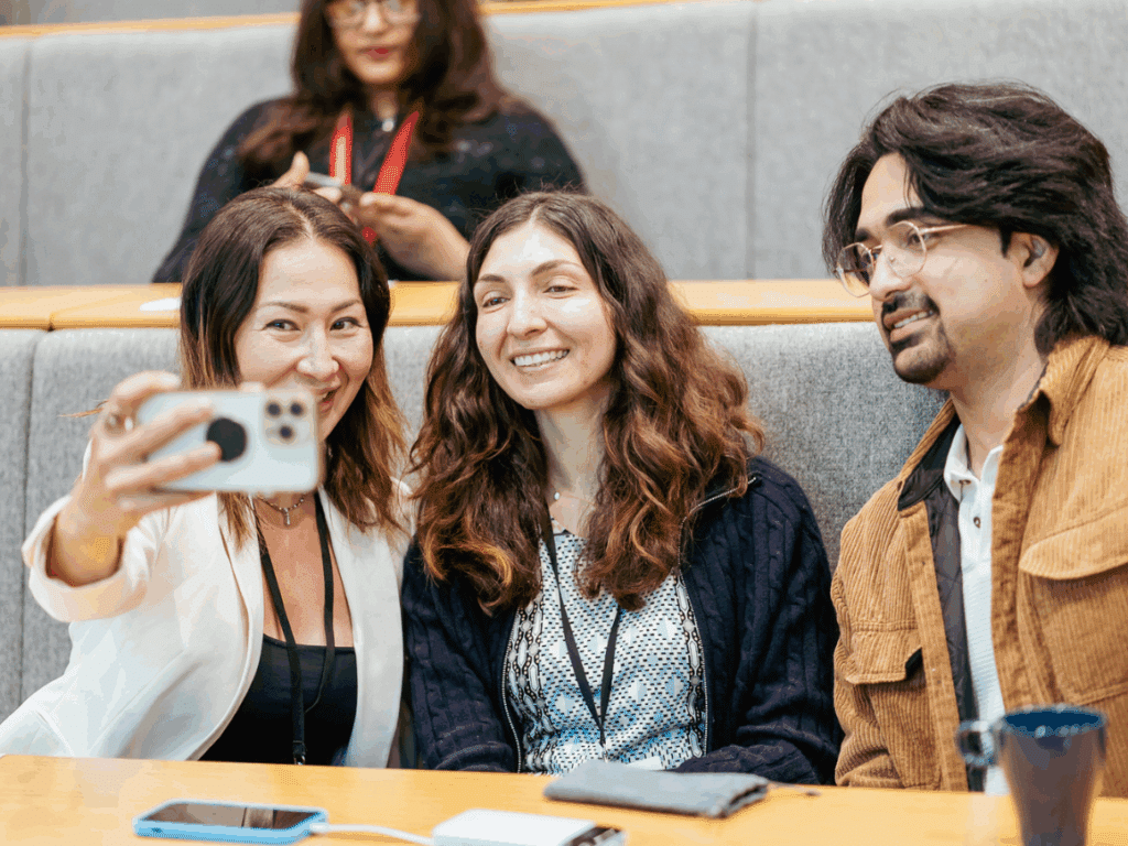 Two women and a man sitting in a lecture hall talking a selfie
