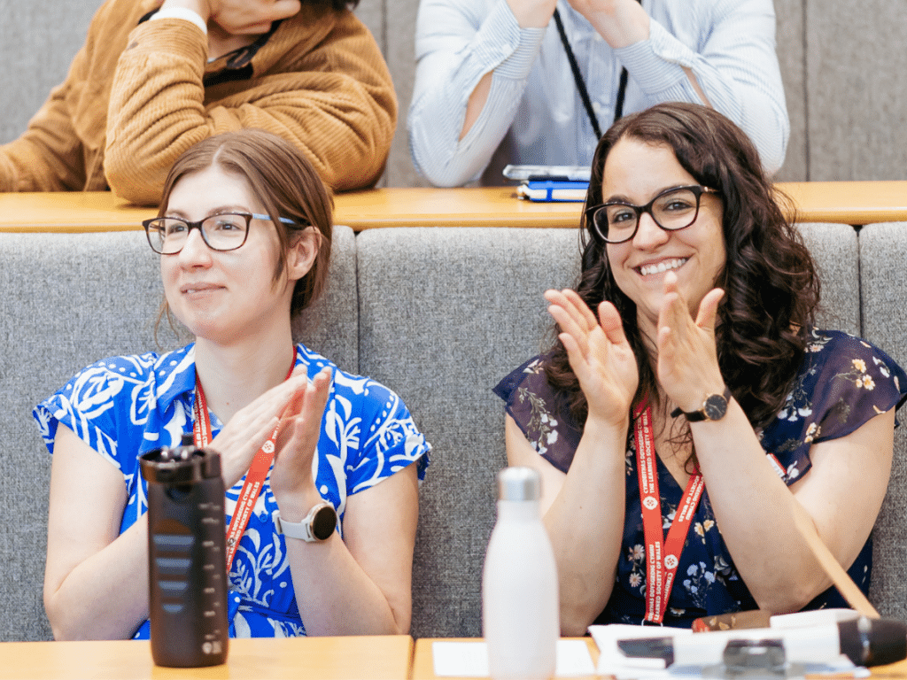 Two women in a lecture hall smiling and applauding.
