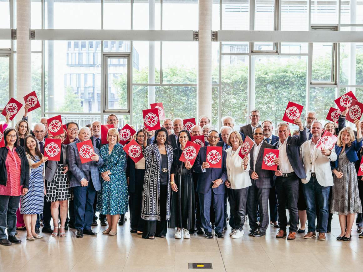 Several dozen Fellows of the Learned Society of Wales in a group facing the camera, some holding brochures in the air with the LSW logo.
