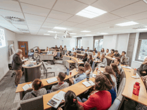 A full seminar room with the audience at semi-circular rows of desks listening to a man speaking.