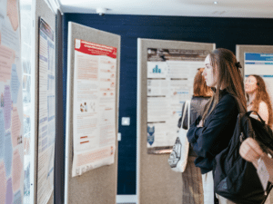 A woman looking at a poster presentation, with several other posters in the background.