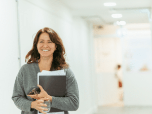 A woman smiling and holding a folder as she walks down a corridor.
