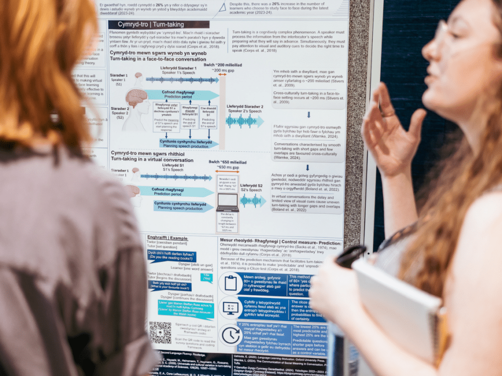 A women standing in front of a poster describing its content to someone off camera.