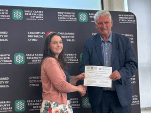 A man and woman shaking hands while he presents her with a certificate.