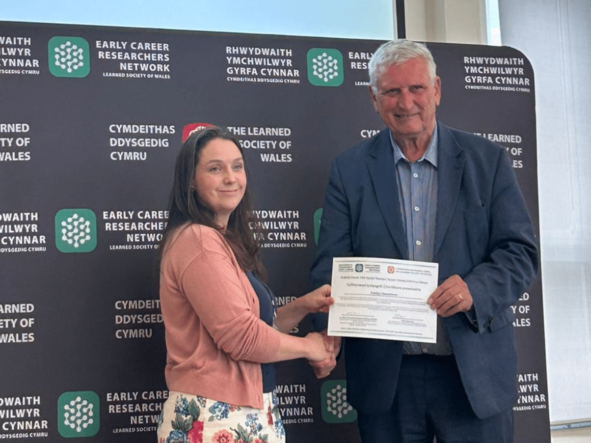 A man and woman shaking hands while he presents her with a certificate.