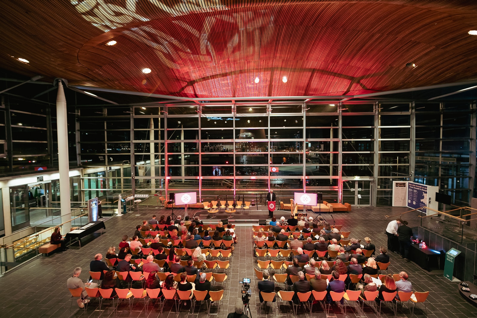 The inside of the Senedd with rows of seats in the main hall and a man talking at a lectern.