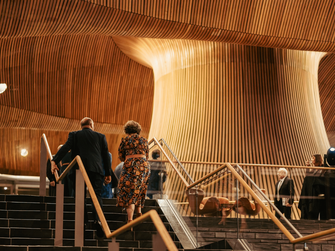 A man and a woman, photographed from behind, walking up the staircase at the Senedd.